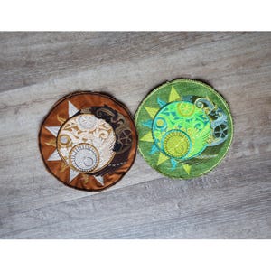May include: Two embroidered patches, one with a brown background and a white sun and moon design, and the other with a green background and a green sun and moon design.