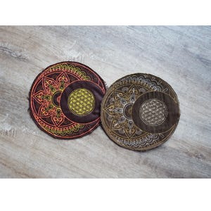 Può includere: Due sottobicchieri rotondi in tessuto con intricati disegni di mandala. Un sottobicchiere presenta un mandala giallo e arancione con un motivo floreale, mentre l'altro presenta un mandala dorato e bianco con un motivo floreale.