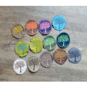 Könnte beinhalten: Eine Sammlung gestickter Aufnäher mit einem Baumdesign. Die runden Aufnäher zeigen einen gestickten Baum in verschiedenen Farben, darunter Gelb, Orange, Pink, Blau und Grün. Die Aufnäher sind auf einer Holzoberfläche angeordnet.