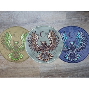 Könnte beinhalten: Drei runde gestickte Aufnäher mit einer Eule mit ausgebreiteten Flügeln. Die Aufnäher sind in Grün, Braun und Blau.