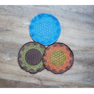 May include: Three round fabric coasters with a flower of life design. The coasters are blue, brown, and orange.