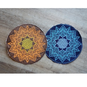 Puede incluir: Dos tapices redondos de tela bordada con diseños de mandalas. El de la izquierda es marrón con un mandala naranja y el de la derecha es azul con un mandala turquesa.