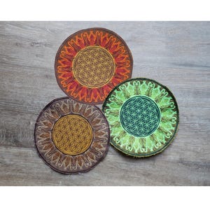 May include: Three circular embroidered patches featuring a central flower of life geometric pattern surrounded by a stylized petal border. One patch is orange and red, one is brown and gold, and one is green and light green with dark edges.