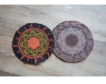 May include: Two round, embroidered fabric patches with a mandala design. The left patch has a yellow and orange mandala with a black background. The right patch has a white mandala with a brown background.