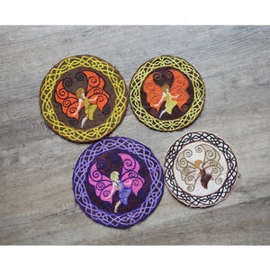 May include: Four embroidered circular coasters with a fairy design. Two coasters have a brown background with orange and yellow accents. One coaster has a purple background with pink accents. The last coaster has a white background with brown accents.