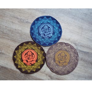 Puede incluir: Tres parches redondos de tela con un diseño de mandala bordado que presenta una deidad en el centro. Los mandalas son en tonos de azul, naranja y beige.