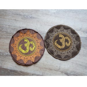 May include: Two round brown fabric patches with intricate gold embroidery. The center of each patch features a stylized Om symbol.
