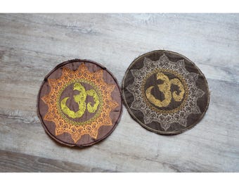 May include: Two round brown fabric patches with intricate gold embroidery. The center of each patch features a stylized Om symbol.
