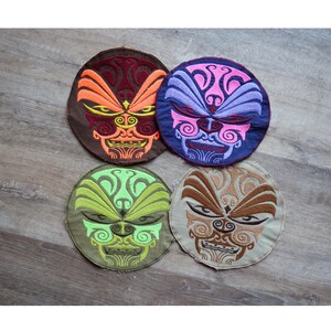 Peut inclure: Quatre écussons brodés circulaires avec des motifs de visages stylisés. Chaque écusson présente une palette de couleurs différente : marron et orange, violet et rose, vert et jaune, et beige et marron. Les écussons sont détaillés et texturés.