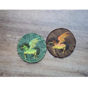 May include: Two round embroidered patches featuring a winged unicorn design. One patch is green with a lime green unicorn, and the other is brown with a yellow and orange unicorn. The patches have a distressed, vintage look.