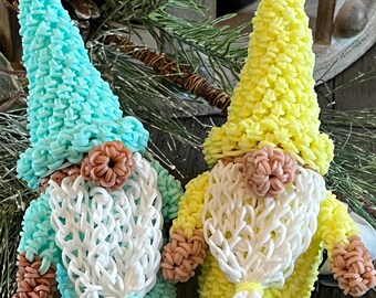 May include: Two handmade gnome figurines. One gnome is turquoise with a white beard and a brown nose. The other gnome is yellow with a white beard and a brown nose. Both gnomes have a looped design.