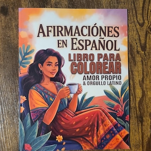 May include: A book cover with the title "Afirmaciones en Español Libro Para Colorear" featuring an illustration of a woman holding a cup. The woman is wearing a colorful dress and is seated in a chair. The book's theme is self-affirmation and Latino pride.