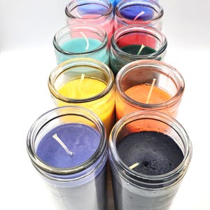 May include: A set of 12 glass jar candles in various colors, including blue, pink, green, yellow, orange, purple, and black. The candles are arranged in a row, with the tops of the jars facing the viewer. Each candle has a single wick.