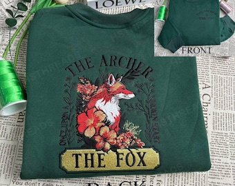 May include: A dark green crewneck sweatshirt featuring an embroidered design of a red and white fox surrounded by red flowers. The text reads THE ARCHER, THE FOX, ONCE UPON A, and BROKEN HEART. The front shows the text THE ARCHER & THE FOX.