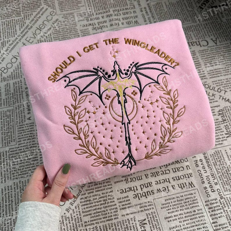May include: Pink sweatshirt with embroidered text that reads "Should I get the Wingleader?" and a gold embroidered dragon with wings and a tail.