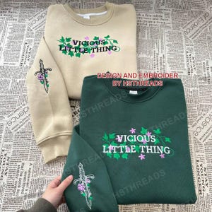 Pu&ograve; includere: Due felpe con disegni ricamati. Una &egrave; beige con un tralcio verde e un pugnale, e il testo "VICIOUS LITTLE THING". L'altra &egrave; verde scuro con un design simile e lo stesso testo. Entrambe le felpe hanno il testo "DESIGN AND EMBROIDER BY HSTHREADS" sul davanti.
