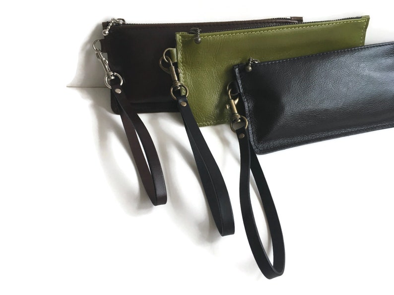 May include: Three leather zippered pouches with wrist straps. The pouches are brown, green, and black.