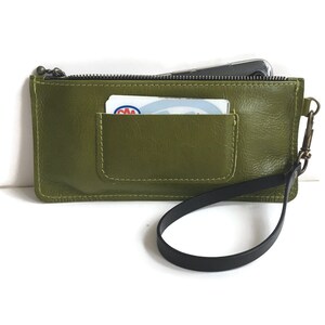 May include: A green leather zippered pouch with a black strap and a small pocket on the front. The pouch has a zipper closure and a small card inside the pocket.