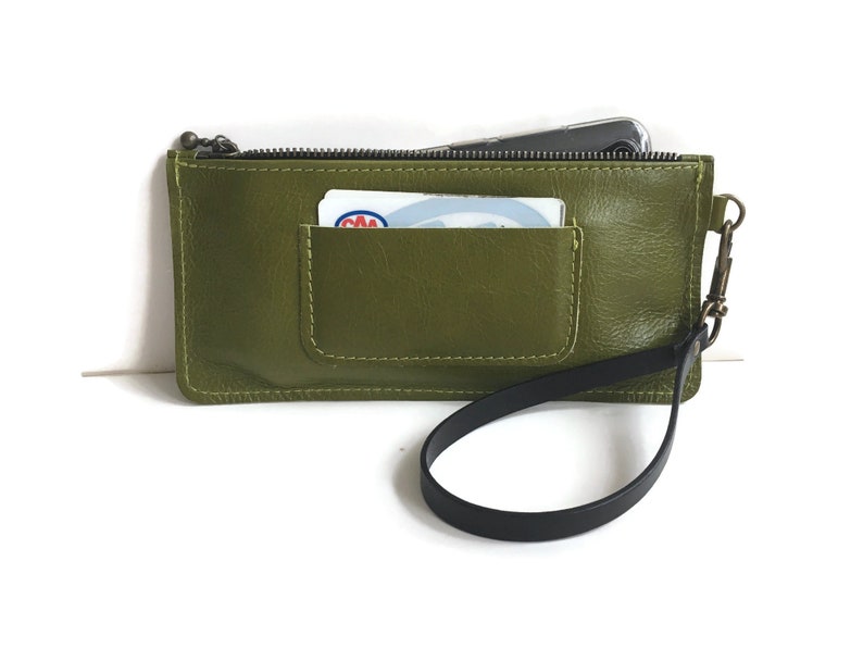 May include: A green leather zippered pouch with a black strap and a small pocket on the front. The pouch has a zipper closure and a small card inside the pocket.