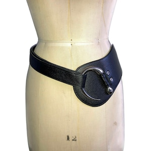 Peut inclure: Une ceinture en cuir noir avec une boucle argentée. La boucle est de forme ovale et a un design incurvé.