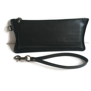 May include: A black leather clutch with a zipper closure and a detachable wrist strap. The strap has a metal clasp.