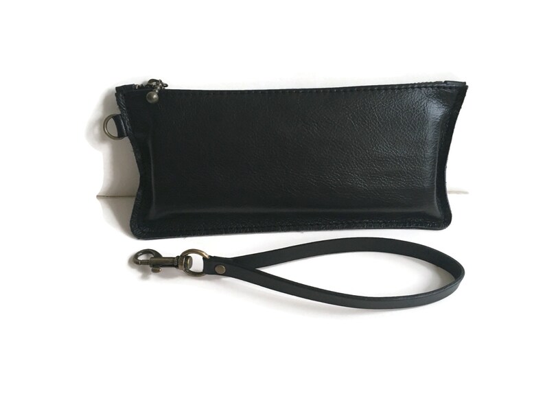 May include: A black leather clutch with a zipper closure and a detachable wrist strap. The strap has a metal clasp.