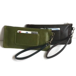 May include: Two leather wallets with wrist straps. One is green and the other is brown. Both have a zipper closure and a small pocket on the front.