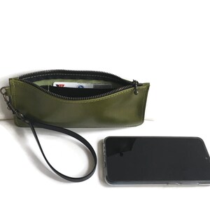 May include: A green leather wristlet with a zipper closure and a black strap. The wristlet is open and a card is visible inside.