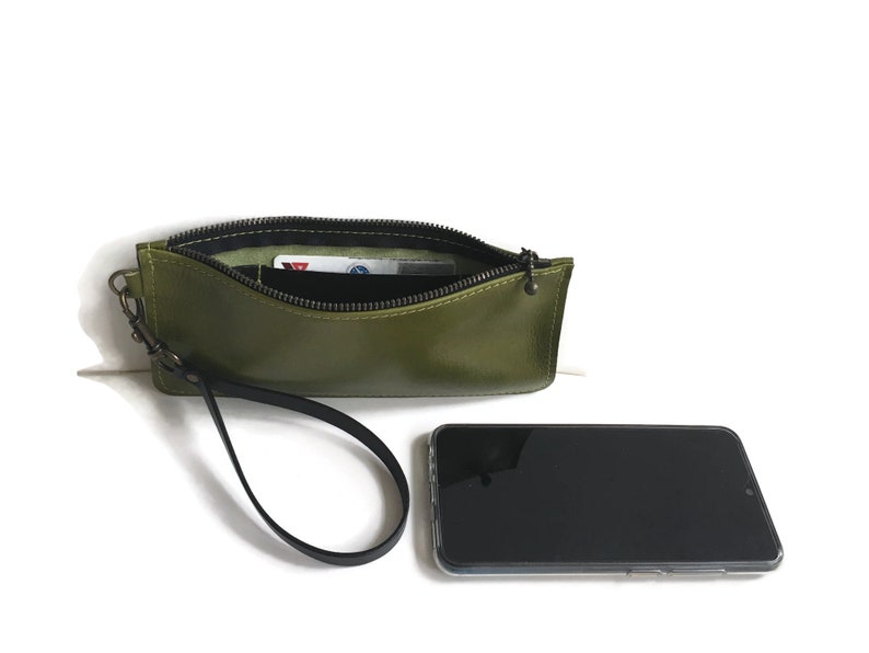 May include: A green leather wristlet with a zipper closure and a black strap. The wristlet is open and a card is visible inside.