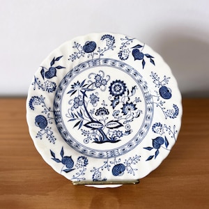 Może przedstawiać: Biały talerz ceramiczny z niebiesko-białym wzorem kwiatowym. Talerz ma falisty brzeg i podwyższony rant.