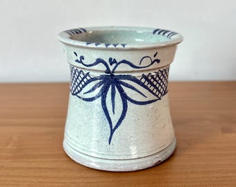 Puede incluir: Un jarrón de cerámica con un acabado moteado azul claro y blanco. El jarrón presenta un diseño de hojas y celosías azul oscuro alrededor del centro y un borde azul oscuro. El jarrón mide aproximadamente 13 cm de alto.