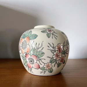 May include: A white ceramic vase with a floral design. The vase is decorated with pink, peach, and green flowers.