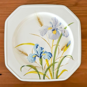 May include: White ceramic dinner plate with a green border and a floral design featuring blue and purple irises and wheat stalks.
