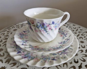 May include: A white teacup and saucer set with a floral pattern in shades of blue, pink, and purple. The cup and saucer have a swirling design.