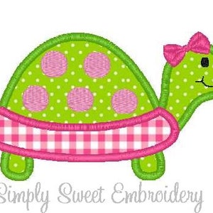 May include: A green and pink embroidered turtle with a pink bow. The turtle has a gingham shell and pink polka dots.