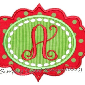 May include: Red and green embroidered monogram with the letter A in a white oval with a green and white striped background. The oval is surrounded by a red scalloped frame with white polka dots.