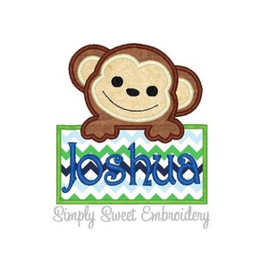 May include: Embroidered design featuring a smiling monkey holding a green, blue, and white chevron banner with the name "Joshua" on it. The design is from Simply Sweet Embroidery.
