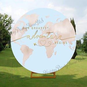 Puede incluir: Un telón de fondo redondo con un mapa del mundo en tonos azul claro y melocotón. La inscripción dorada dice "Our Greatest Adventure Begins" con un corazón y un avión. El telón de fondo está sostenido por un soporte de madera, sobre una hierba.