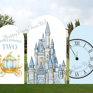 May include: Three arch-shaped party decorations. One features a blue and gold carriage with the text "Bibbidi Bobbidi Two". The center decoration shows a blue and gold castle. The third shows a clock face with the hands at five minutes to twelve.