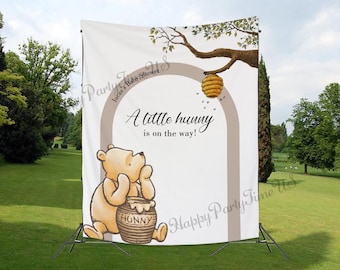May include: A Winnie the Pooh themed baby shower backdrop with a brown archway and the text "A little hunny is on the way!" Winnie the Pooh is standing next to a pot of honey that says "Hunny".