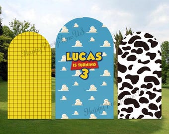 May include: Three arch-shaped cardboard cutouts for a birthday party. The center cutout is blue with white clouds and the text "Lucas is turning 3". The cutout on the left is yellow with a grid pattern. The cutout on the right is white with black cow spots.