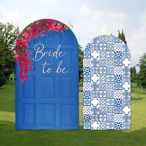 Könnte beinhalten: Zwei gewölbte Aufsteller mit einem blauen Türdesign mit rosa Bougainvillea-Blüten und dem weißen Text Bride to be auf der linken Seite sowie einem blau-weißen Fliesenmuster auf der rechten Seite vor einer grünen Rasenfläche.