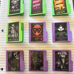 May include: Nine miniature book covers with various titles and authors, including "Nocticadia," "Butcher & Blackbird," and "Scythe & Sparrow." The covers are in shades of green and purple, with black and white illustrations and text. The books are arranged on lined paper.
