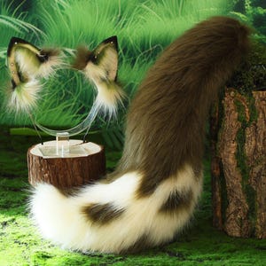 May include: A set of cosplay accessories featuring a brown and white faux fur tail and matching ears on a headband. The ears and tail have a spotted pattern and are displayed on a natural wood base.