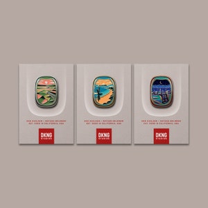 May include: Three enamel pins with different landscape designs. Each pin features a stylized image of a sunset, a beach with a palm tree, and a cityscape with a crescent moon. The pins are all rectangular and have a white background with black text that reads "DKNG Studios".