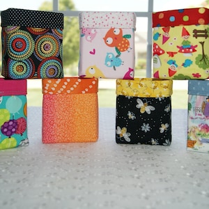 May include: Eight fabric storage bins with different patterns. The bins are all square and have a black, white, and red polka dot pattern on the top. The bins are arranged in two rows of four.