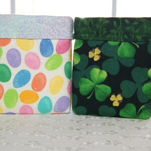 May include: Four fabric storage containers with different patterns. The containers have a rectangular shape with a folded-over top. Patterns include leaves, Easter eggs, shamrocks, and hearts. The tops are solid colors.