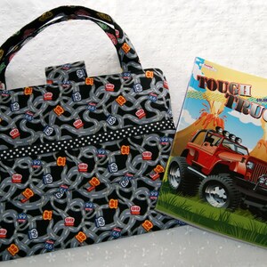 May include: A black and gray tote bag with a road map pattern and white polka dots. The bag has a black handle and a black zipper. The bag is next to a coloring book with a red truck on the cover. The coloring book has the title "Tough Trucks" and the words "Coloring & Activity".