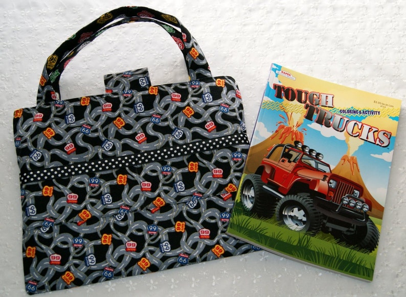 May include: A black and gray tote bag with a road map pattern and white polka dots. The bag has a black handle and a black zipper. The bag is next to a coloring book with a red truck on the cover. The coloring book has the title "Tough Trucks" and the words "Coloring & Activity".