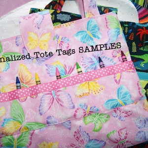 May include: Two personalized tote bags with butterfly patterns. One bag is pink with a butterfly pattern and has a name tag that says "Gwenyth". The other bag is black with a dinosaur pattern and has a name tag that says "Conner". Both bags have a ribbon with white polka dots and are labeled "Personalized Tote Tags SAMPLES".